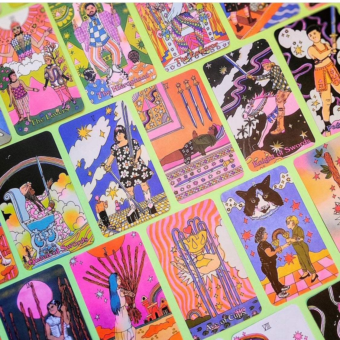 Examples of cards from Queer Tarot: An Inclusive Deck & Guidebook. All are illustrated in bright, groovy colors and feature characters based on real models representing a full range of gender and sexual identities, races, ethnicities, and abilities. Cards pictured include The Lovers, The Hierophant, The Emperor, Queen of Swords, 5 of Swords, 4 of Swords, Knight of Swords, Page of Swords, 9 of Wands, 10 of Wands, Ace of Cups, and 2 of Cups.