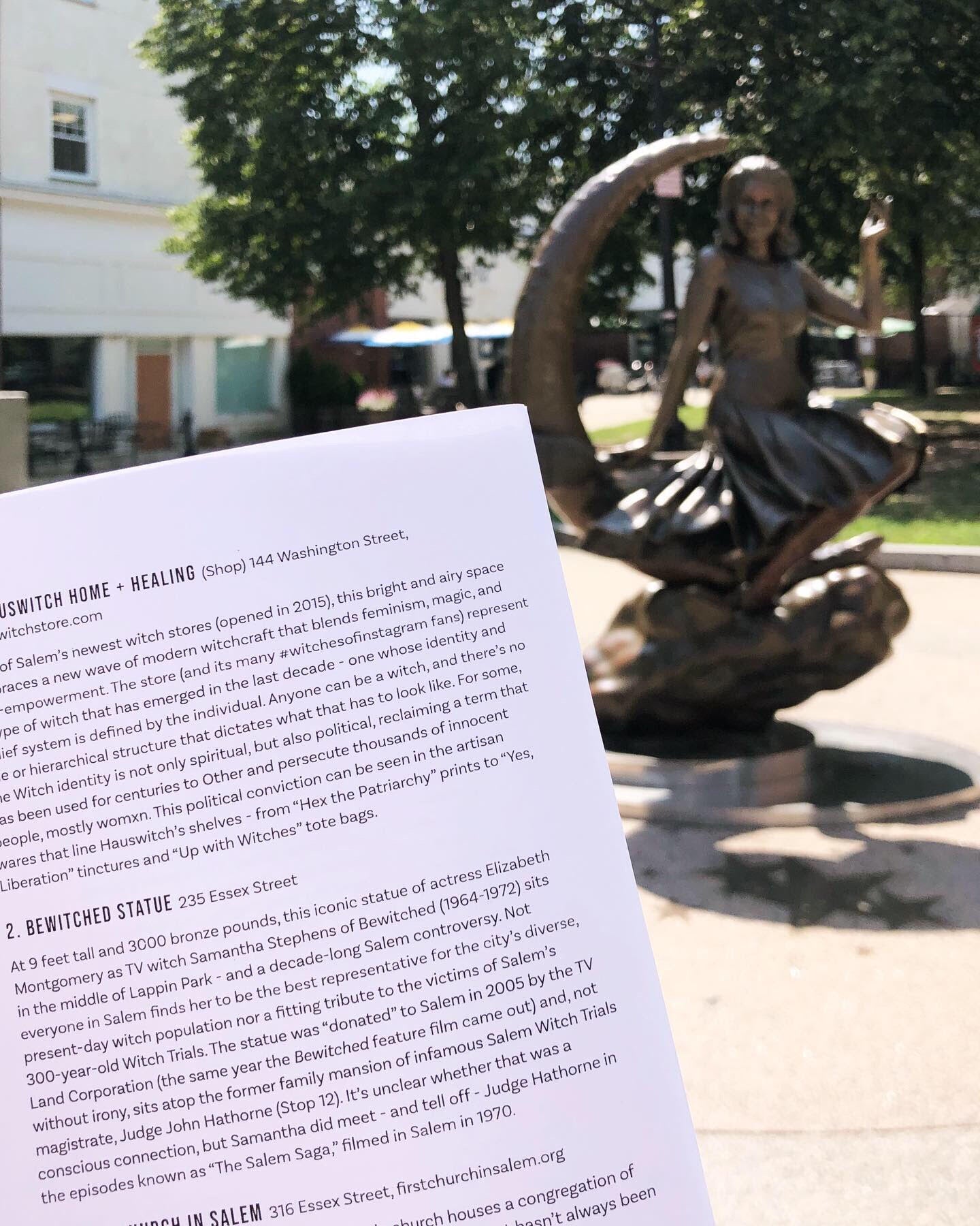 Salem's famous bronze statue of a witch in a dress perched sideways on a crescent moon. In the foreground is a page from Walking the Witch Trials: A DIY Tour of Salem History. Blurbs of text describe HausWitch Home + Healing at 144 Washington Street and the pictured Bewitched Statue at 235 Essex Street.